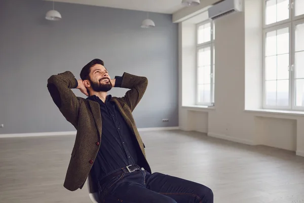 Ein Mann im Geschäftsmann-Anzug entspannt sich in einem Büro, die Hände hinter dem Kopf. — Stockfoto