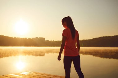 A young girl in training warm up at sunrise by the lake in autumn.