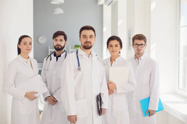 Eine Gruppe selbstbewusst praktizierender Ärzte in weißen Kitteln lächelt vor der Kulisse der Klinik. — Stockfoto