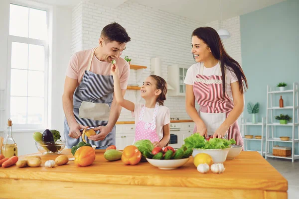 Familia feliz con el niño preparando verduras frescas en la mesa en la cocina . — Foto de Stock