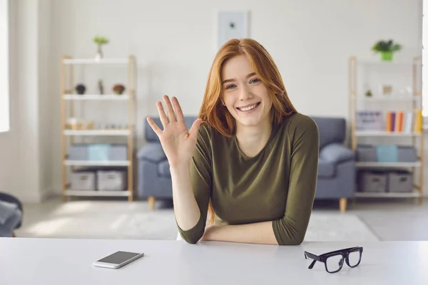 Online video call. Happy girl looking at the camera smiling gretting her hand waving friends sitting at home. — Stock Photo, Image