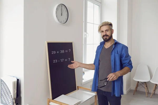 Online education. Male teacher teaches looking at the camera video chat call lesson at the blackboard in the classroom.