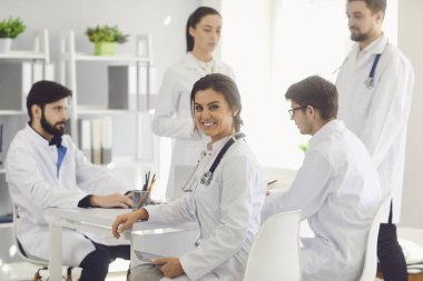 Tıp hastanesinde beyaz önlüklü meslektaşlarıyla aynı masada oturan kadın doktor..