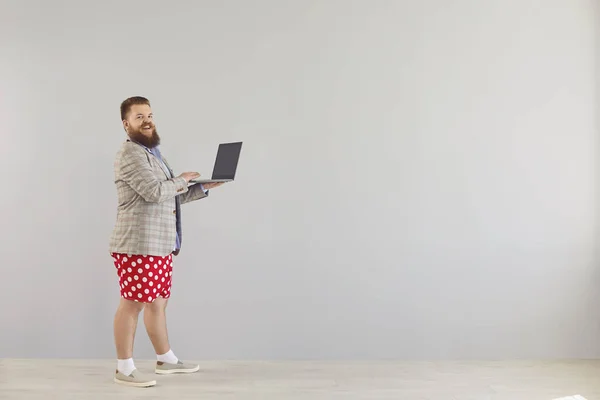 Lustiger dicker Mann in blauem Hemd und roter Hose, der mit einem Laptop auf grauem Hintergrund online arbeitet. — Stockfoto