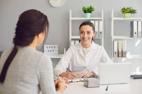 Una paciente visitando a una doctora en el consultorio. Trabajo médico escribe una receta en una mesa en un hospital . —  Fotos de Stock