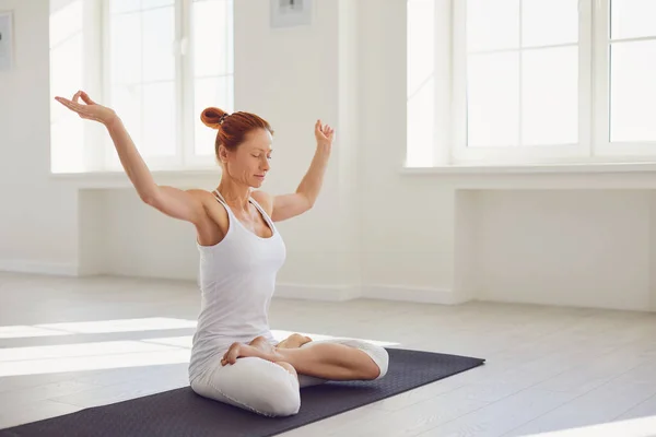 Yoga girl. Fitness woman in white sportswear sitting in a yoga pose meditates relaxes sitting on the floor in a white classroom. — Stockfoto