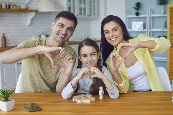 Счастливая улыбающаяся семья держит руки в форме сердца приветствует сидя за столом в кухне в доме — стоковое фото