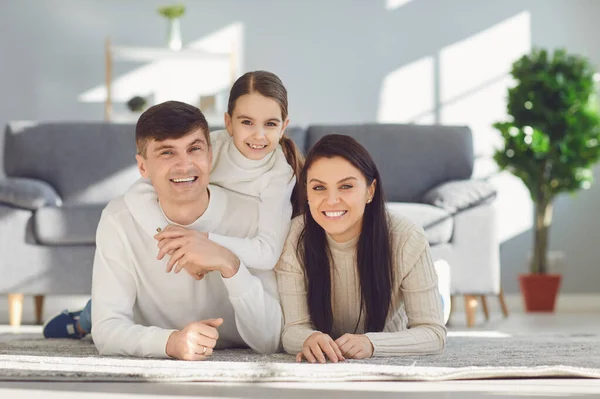Gelukkig glimlachende familie knuffelen terwijl liggend op de vloer in de kamer thuis. C — Stockfoto