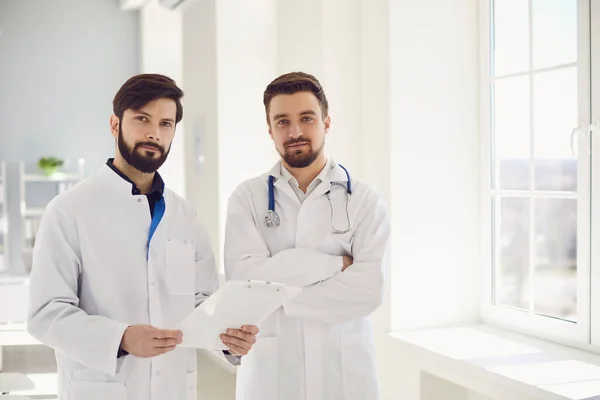 Two practicing doctors with clipboard standing in a clinic office.
