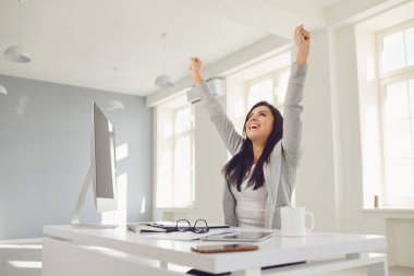 Happy successful smiling business woman raised her hands up while sitting at a table in the office. clipart