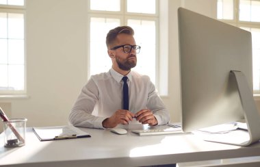Ofiste bilgisayarlı bir masada oturmuş belgelerle uğraşan ciddi bir iş adamı..