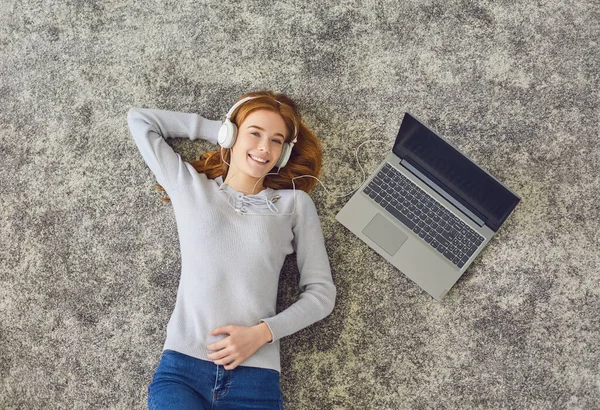 Happy young woman listening to music on gray floor — Stock Photo, Image