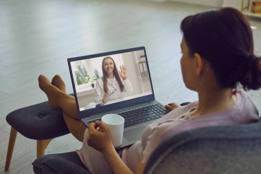 Doktor hatta. Arkadan bakan kadın dizüstü bilgisayarında video danışmanı izliyor. Evde oturuyor..