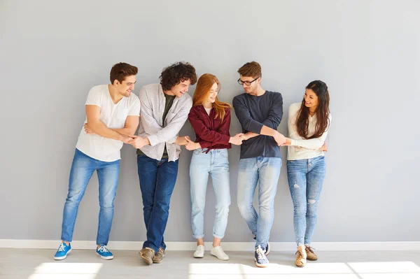 Grupp av unga människor som håller händerna skrattar mot grå bakgrund. — Stockfoto