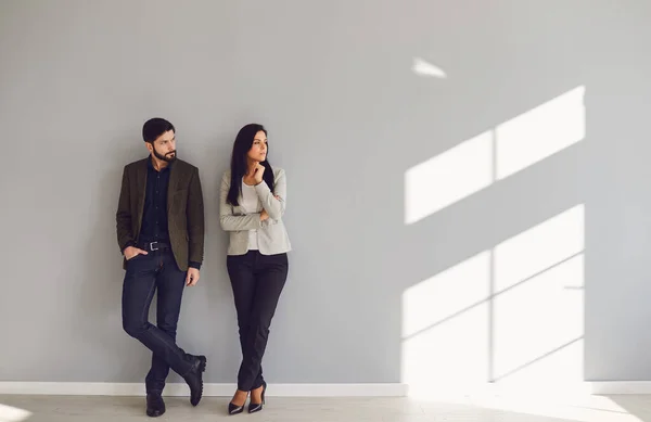 A businessman and a business woman are standing against a gray wall — Stockfoto