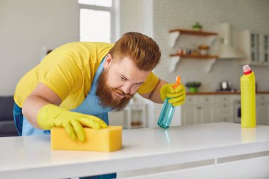 Önlüklü, sakallı komik şişman adam evdeki odayı temizliyor..