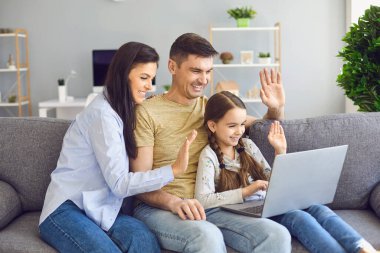 Evdeki kanepede çocukla otururken bilgisayarla mutlu bir aile iletişimi.
