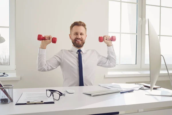 Happy successful businessman in a white shirt does exercises with dumbbells in the office. — Stock Photo, Image