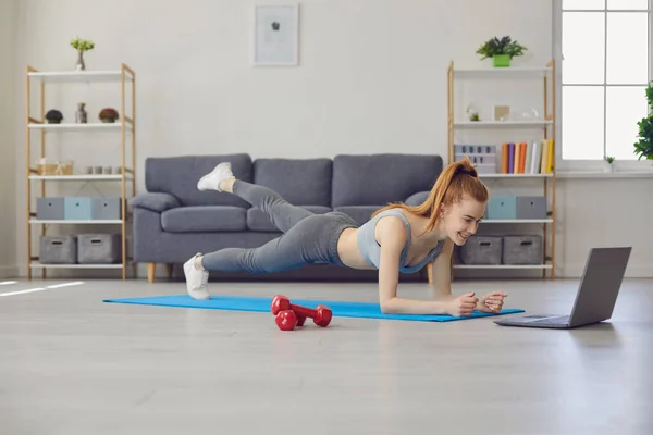 Ćwiczenia w domu online. Dziewczyna robi ćwiczenia na podłodze oglądając kurs wideo za pomocą laptopa w domu. — Zdjęcie stockowe