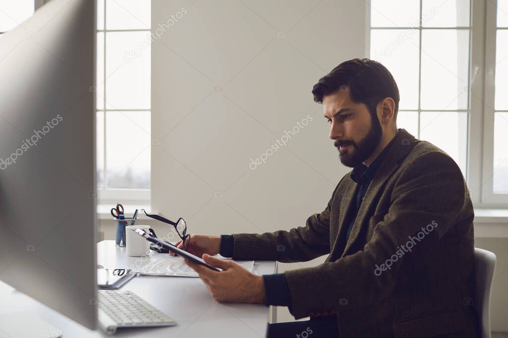 Businessman worker with a beard works in computer behind the workplace in the office.