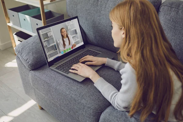 Doctor en línea. Chica paciente escucha video consulta llamada de chat con médico femenino sentado remotamente en el sofá en casa . — Foto de Stock