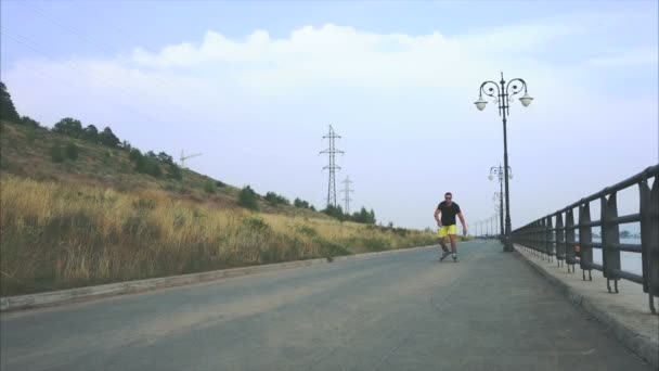 Молодой спортсмен со встроенными коньками катается и прыгает на летней набережной — стоковое видео