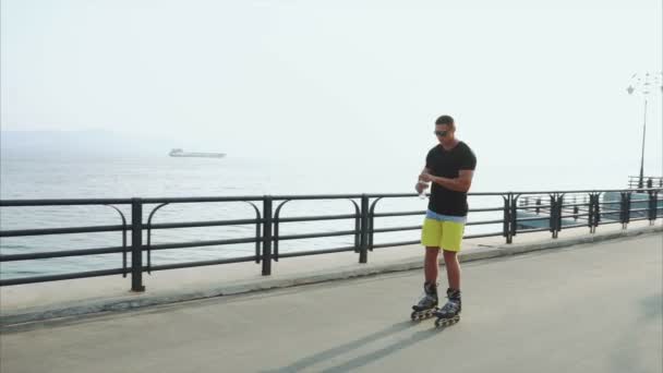 Jeune homme sportif patinage à roulettes et boire de l'eau de la bouteille sur le front de mer — Video