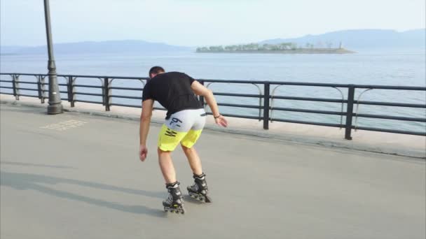 Young sporty man learns to roller skate and jump on waterfront — Stock Video