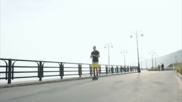 Młody człowiek sportowy roller skating i napił się wody z butelki na nabrzeżu — Wideo stockowe