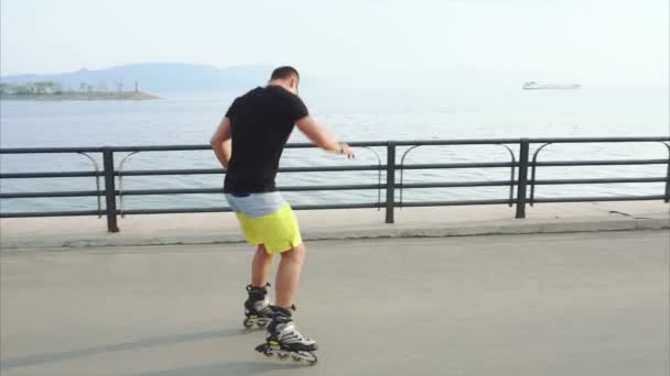 Ung sportig man lär sig att roller skate och hoppa på waterfront — Stockvideo