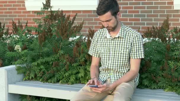 Casual dressed man sit on the bench and use his smartphone — Stock Video