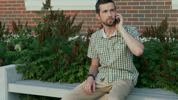 Casual dressed man sit on the bench and call to his friend using smartphone — Stock Video