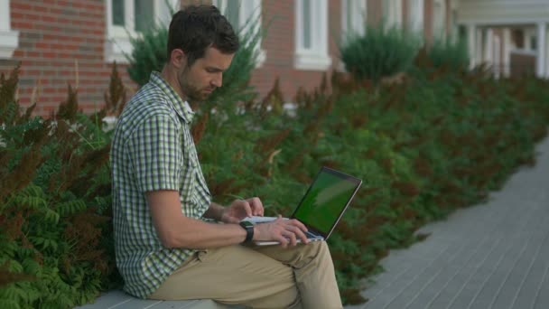 Casual uomo vestito freelance sedersi sulla panchina e utilizzare il suo smartwatch e laptop — Video Stock