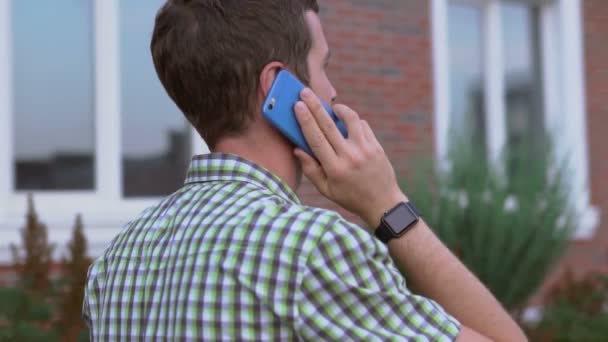 Young man wearing smartwatch walking on the street and talking by smartphone — Stock Video