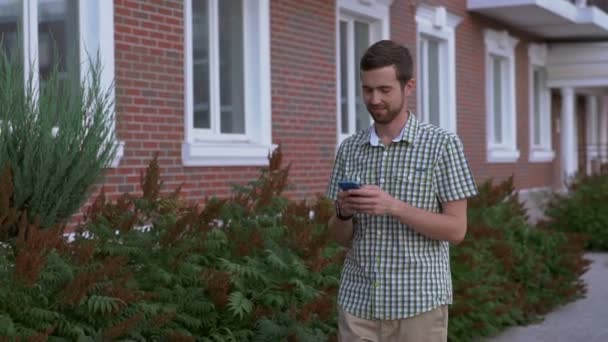 Smartwatch 的年轻人走在街上，并用他的智能手机，微笑着 — 图库视频影像
