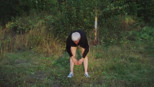 Viejo hombre mayor hace ejercicios de calentamiento por la mañana antes de correr — Vídeo de stock