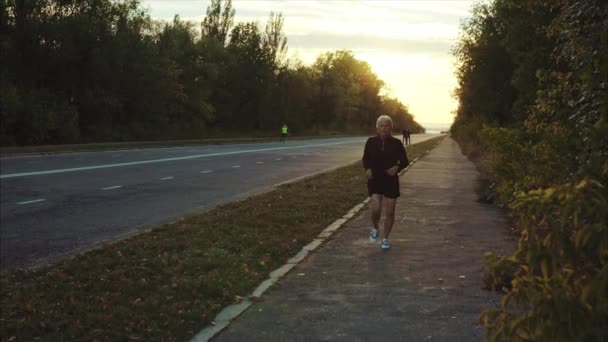 Senior uomo dai capelli grigi jogging sulla strada della città tramonto — Video Stock
