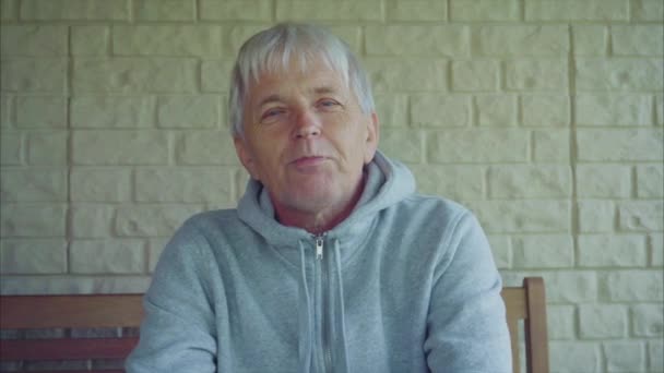 Портрет пожилого мужчины, седые волосы снаружи дома, сидящего на скамейке — стоковое видео
