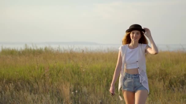 Young beautiful girl model in hat walking and posing on meadow near the river — Stock Video