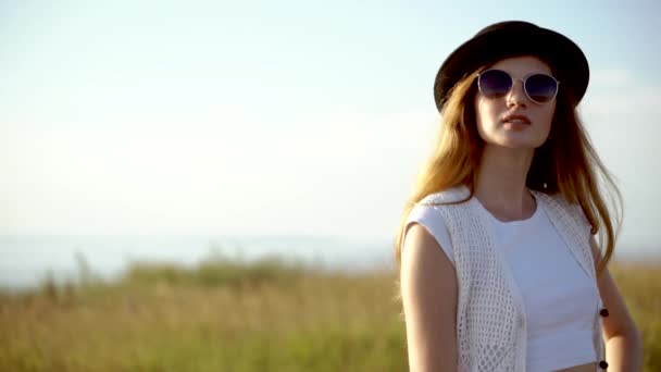 Joven hermosa mujer modelo en sombrero y gafas de sol posando en cámara lenta al aire libre — Vídeo de stock
