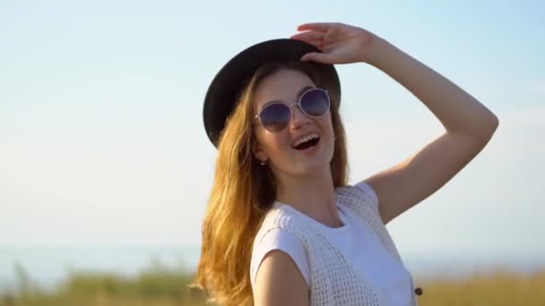Jeune belle femme modèle en chapeau et lunettes de soleil posant et souriant en plein air — Video