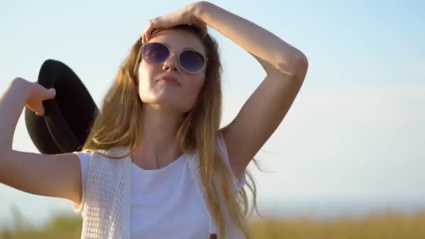 Jeune belle femme modèle en chapeau et lunettes de soleil posant et souriant en plein air — Video