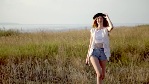 Молодая красивая девушка модель в шляпе runnig и танцы на лугу у реки — стоковое видео