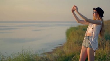 Genç kadın güzel bir günbatımı manzarası video çekim için bir akıllı telefon kullanır