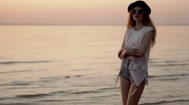 Şapkalı genç sarışın kız okyanus ve altın günbatımı arka plan üzerinde yürümek