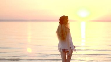 Doğa ve günbatımı keyfini deniz kenarında yürüyen genç kadın