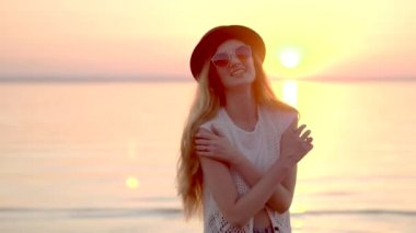 Genç ve güzel kız şapka ve güneş gözlüğü altın günbatımı arka plan üzerinde poz