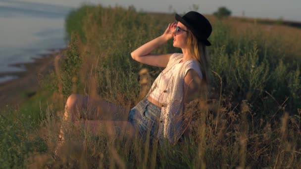 Mujer joven con gafas de sol sentada en el borde de un acantilado disfrutando de la naturaleza — Vídeos de Stock
