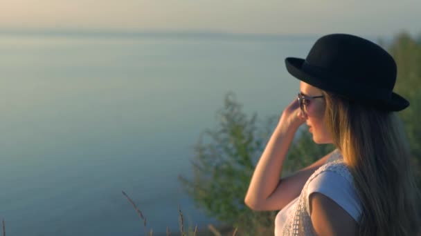 Ung kvinna i solglasögon sitta på kanten av en klippa som njuter av naturen — Stockvideo