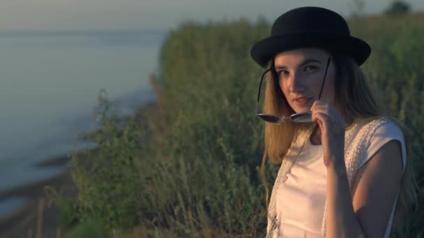 Junge Frau mit Sonnenbrille sitzt am Rande einer Klippe und genießt die Natur — Stockvideo